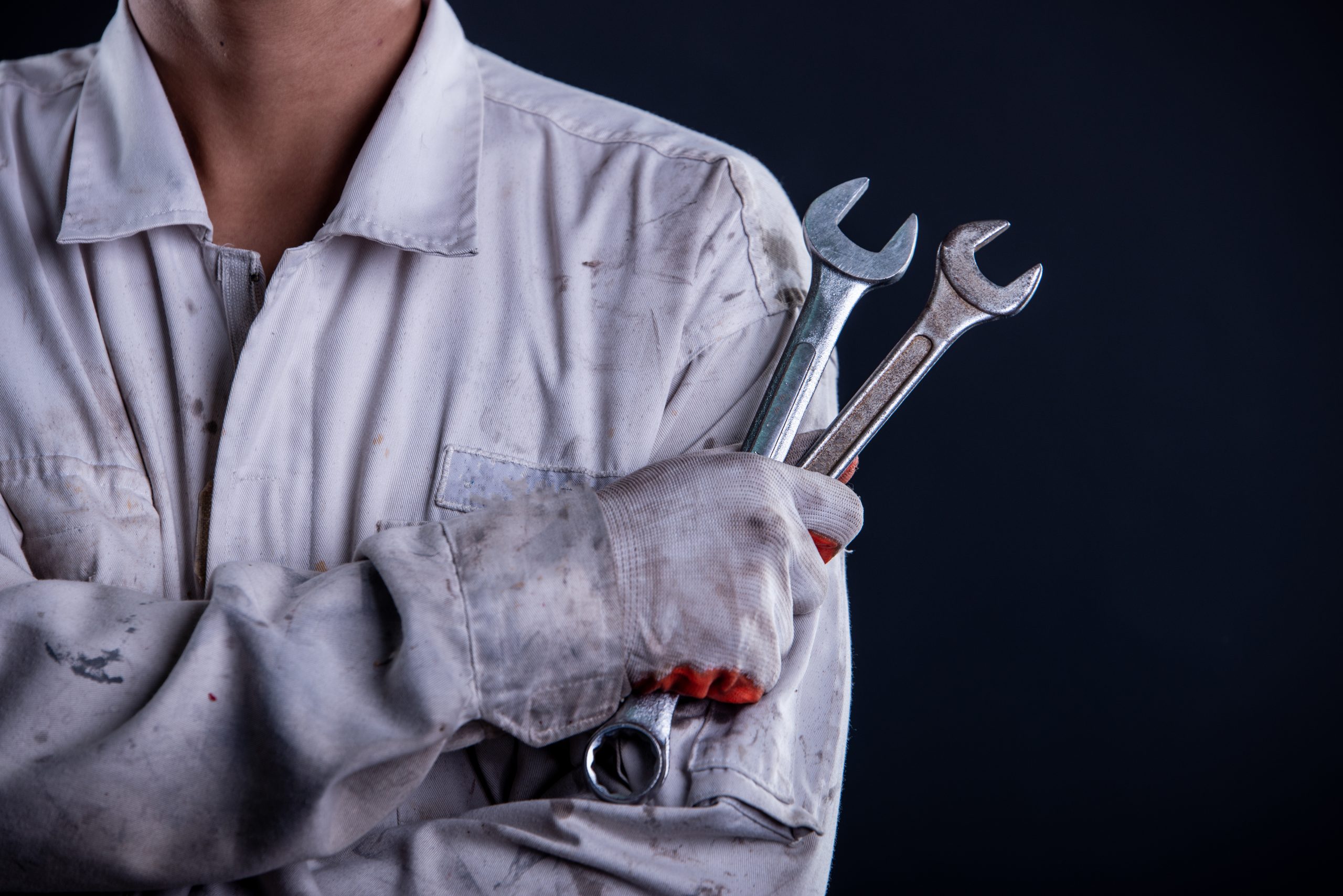 Car mechanic wearing a white uniform stand holding wrench isolated on gray background with copy space.